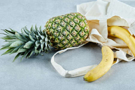 Ripe pineapple and banana in a white bag on blue background
