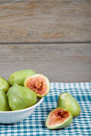Green figs in a white bowl and on a wooden table with blue tableclothの写真素材
