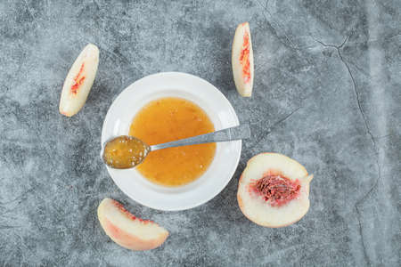A white plate with jam and peaches on a gray tableclothの写真素材