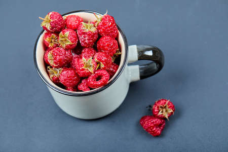 Fresh red raspberries in mug on blue background