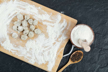 Raw dumplings on a wooden board with bowl of flourの写真素材