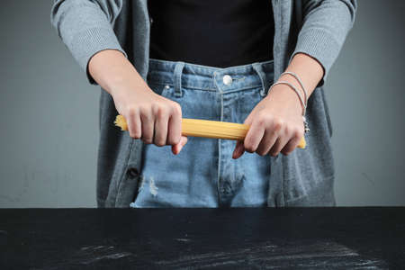 Woman breaking raw spaghetti on dark tableの写真素材