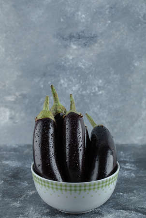 Vertical photo of Pile of organic eggplants in bowl on grey backgroundの写真素材