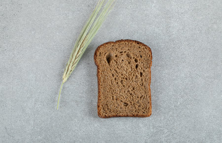 A slice of brown bread with wheat on a gray backgroundの写真素材