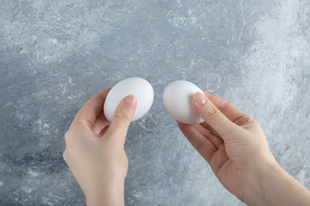 Female hand holding two eggs on grey background
