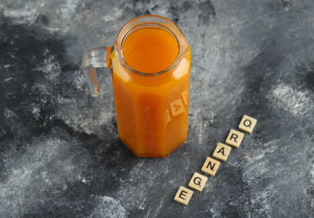 Jug of orange juice with wooden letters on marble backgroundの写真素材