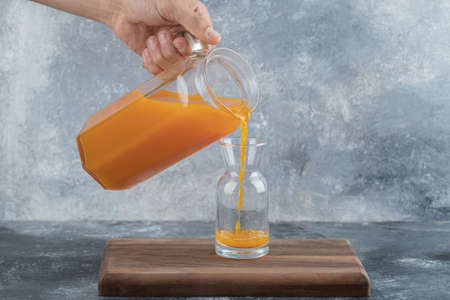 Male hand pouring orange juice into glassの写真素材