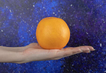 Female hand holding orange on blue backgroundの写真素材