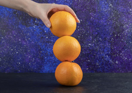 Female hand holding three oranges on blue background