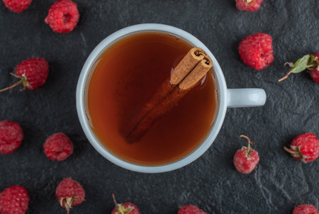 Cup of tea and fresh raspberries on black background