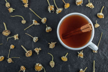 Cup of tea with cinnamon and pile of dried chamomiles