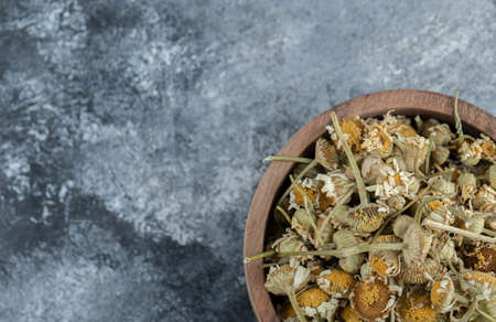 Wooden bowl of dried chamomile on marble backgroundの写真素材