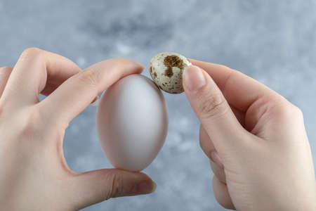 Female hand holding two eggs on grey backgroundの写真素材