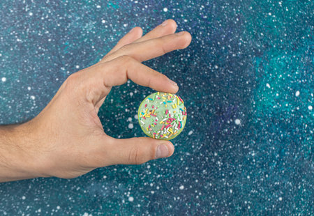 Male hand holding green cookie with colorful candies