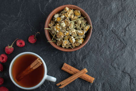 Cup of tea with raspberries and chamomile on black backgroundの写真素材