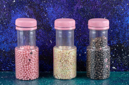 Three plastic bottles of sprinkles and candies on blue backgroundの写真素材