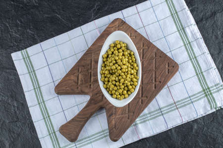 Top view of marinated green olives in white bowl over wooden cutting board