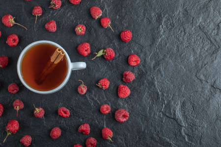 Cup of tea and fresh raspberries on black background