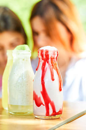A milkshake and two lemonades on wooden table in front of two women