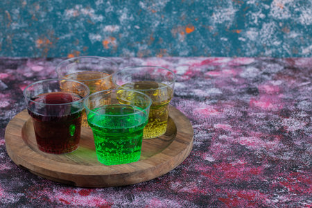Multicolor drinks in plastic cups on a wooden platterの写真素材