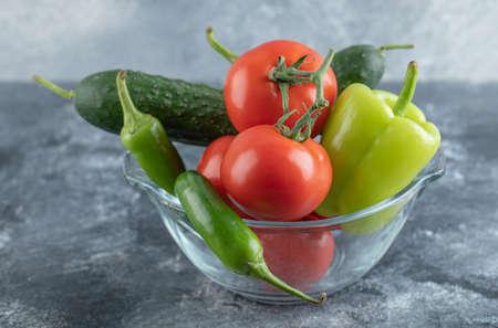 Close up photo of glass bowl full with ripe vegetables over grey background