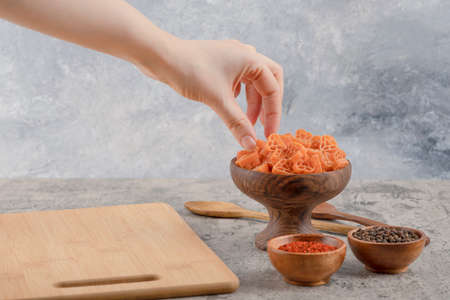 Female hand taking macaroni from wooden bowl on marble backgroundの写真素材