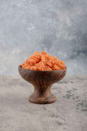 Wooden bowl of raw macaroni placed on marble background