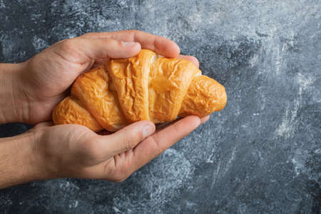 Male hands holding fresh croissant on marble backgroundの写真素材