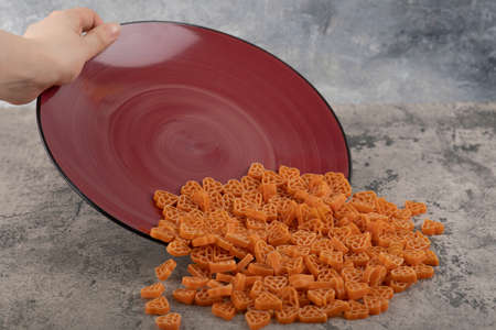 Female hand holding burgundy plate macaroni on marble background