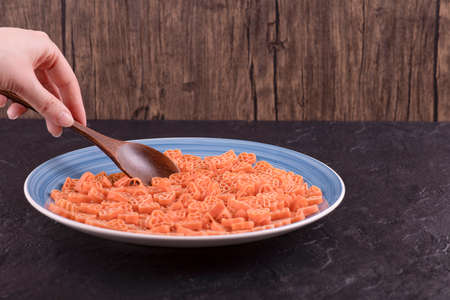 Woman hand taking raw pasta in hearts shape with wooden spoon on black tableの写真素材
