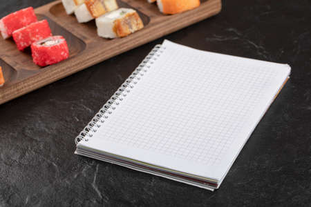 Wooden plate of traditional sushi rolls and notebook on black table