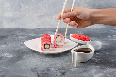 Male hand picking sushi roll with chopsticks on marble background