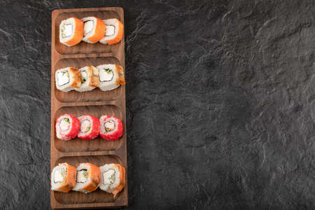 Wooden plate of traditional sushi rolls on black tableの写真素材