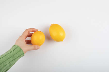 Female hand holding fresh yellow lemon on white background