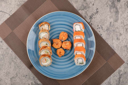 Blue plate of various sushi rolls on marble table