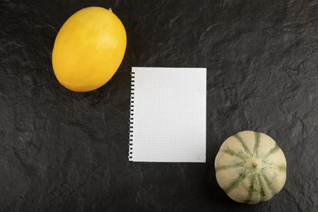 Yellow and gray pumpkin with an empty sheet of paper on black tableの写真素材