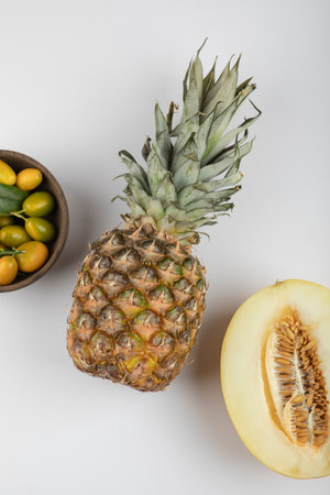 Bowl of yellow kumquats, melon and pineapple on white backgroundの写真素材