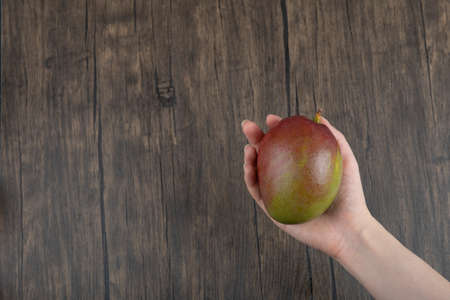 Female hand holding delicious ripe mango on wooden surfaceの写真素材