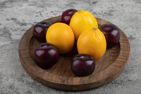 A wooden plate of purple plums and fresh lemons on stone backgroundの写真素材