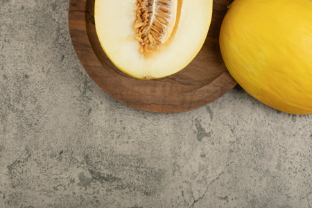 Halved and whole delicious yellow melon on wooden plateの写真素材