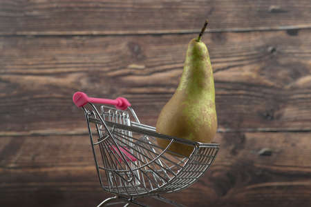 Fresh juicy pear placed in small trolley on wooden background