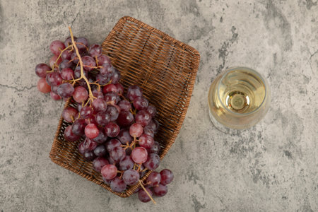Wicker basket of red grapes with glass of wine on marble tableの写真素材