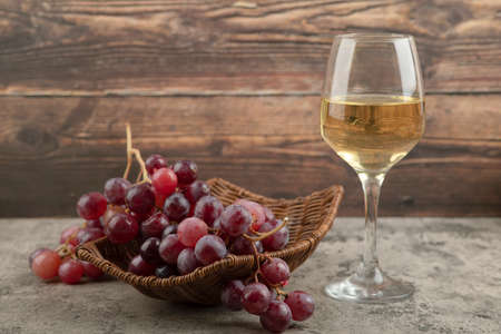 Wicker basket of red grapes with glass of wine on marble tableの写真素材