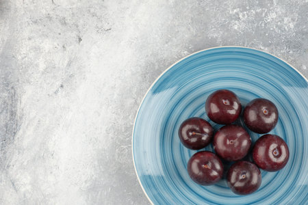 Blue plate of fresh purple plums on marble surface