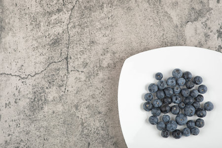 White plate of delicious fresh blueberries on marble surfaceの写真素材
