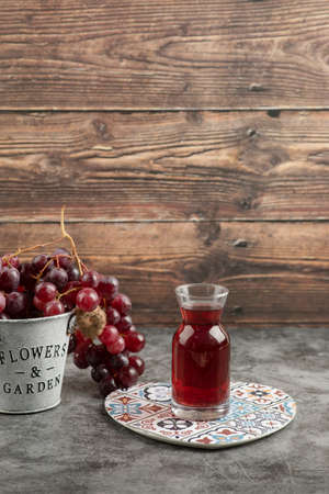Metal bucket of red fresh grapes and glass of juice on marble tableの写真素材