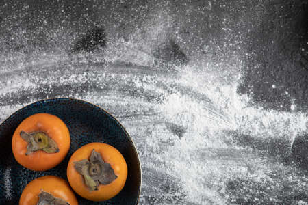 Three ripe persimmon fruits placed on black plate