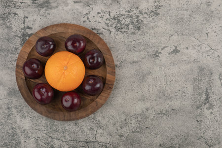 A wooden plate of fresh purple plums with healthy orangeの写真素材