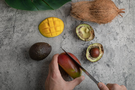 Male hands cutting fresh mango on marble surfaceの写真素材