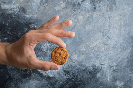 Male hands holding delicious chocolate chip cookies on marble backgroundの写真素材